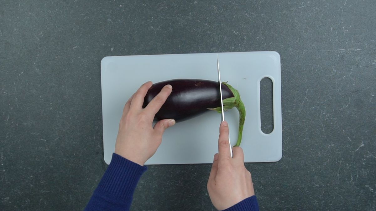 hand cutting eggplant on white cutting board