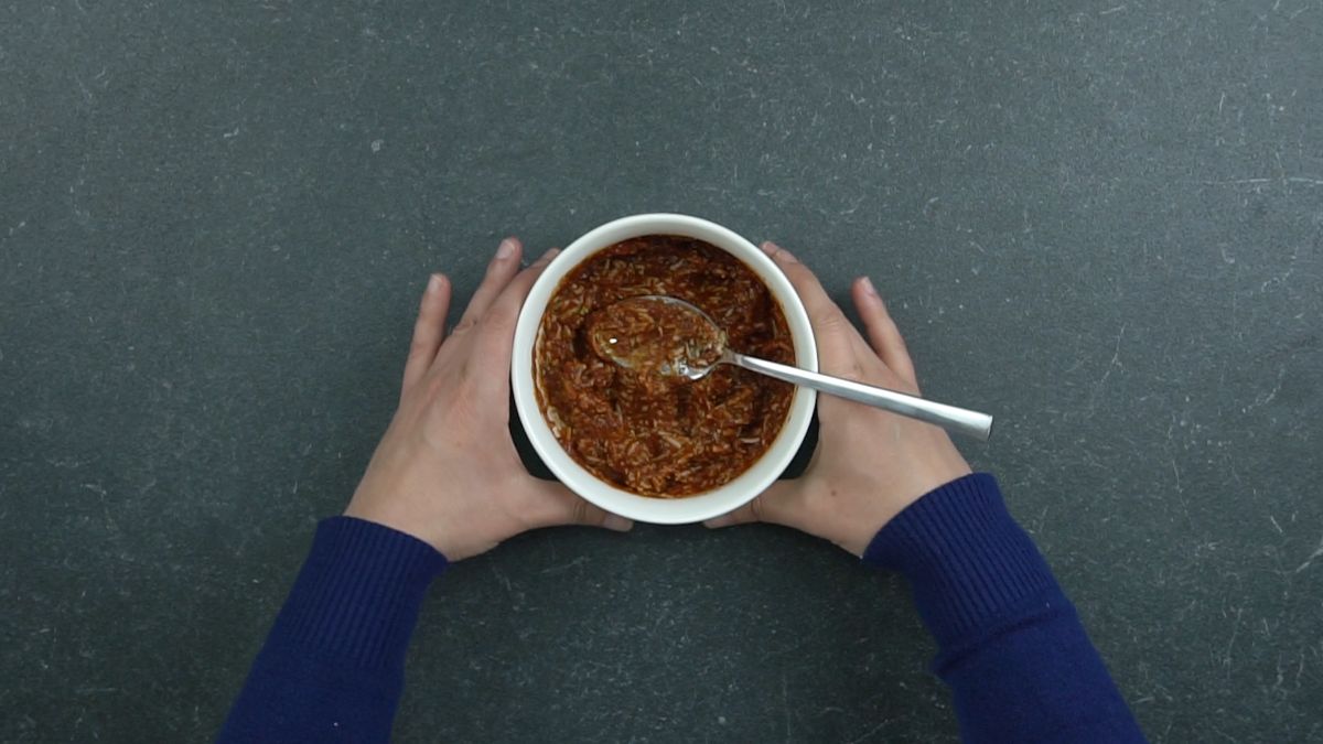 hands holding white bowl of pasta sauce