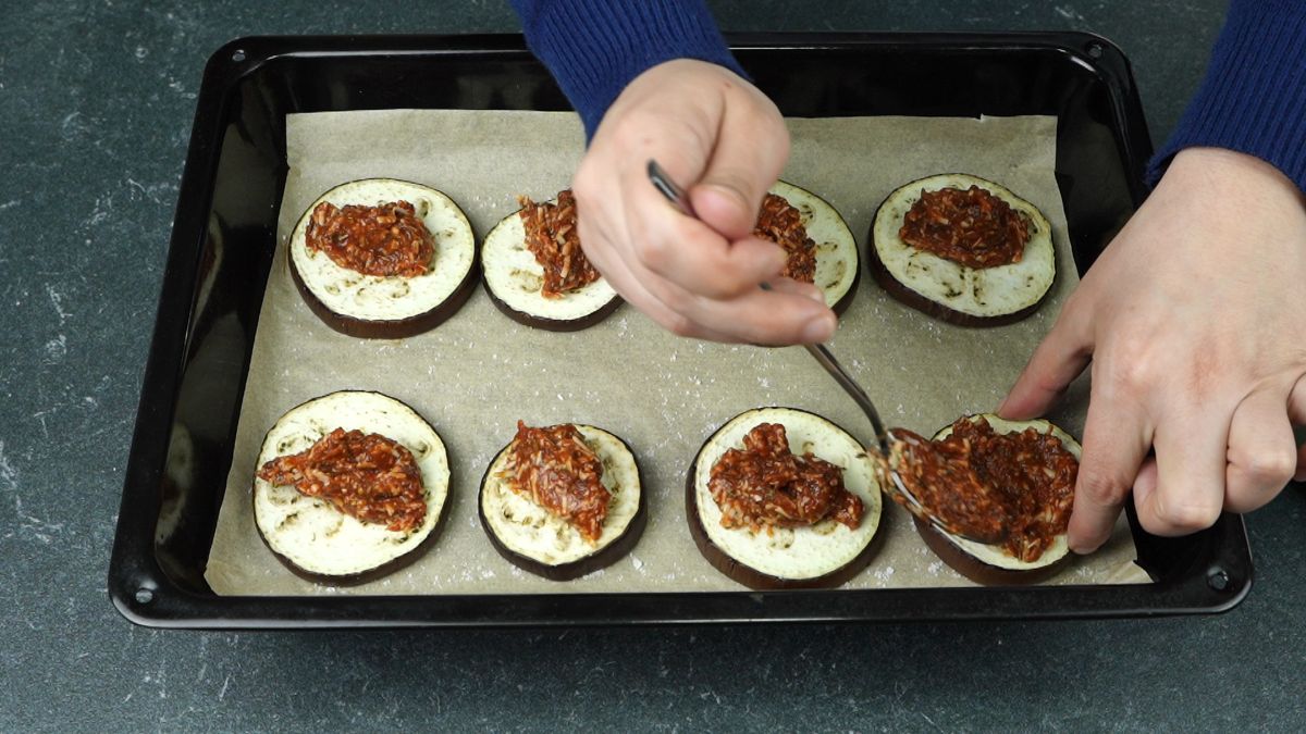 hand spooning sauce onto eggplant rounds