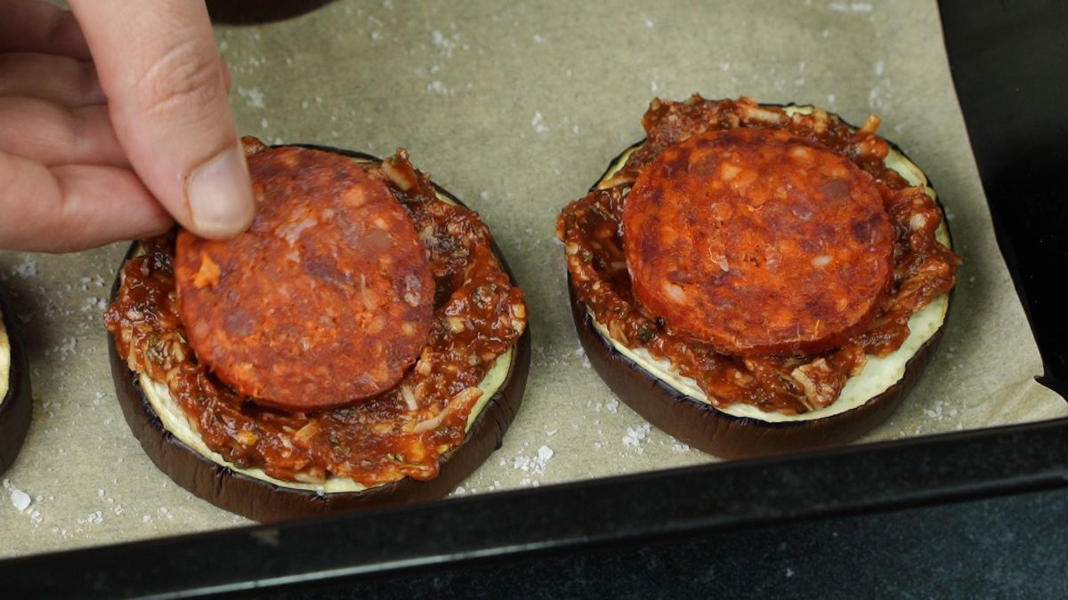 hand putting pepperoni on top of eggplant round