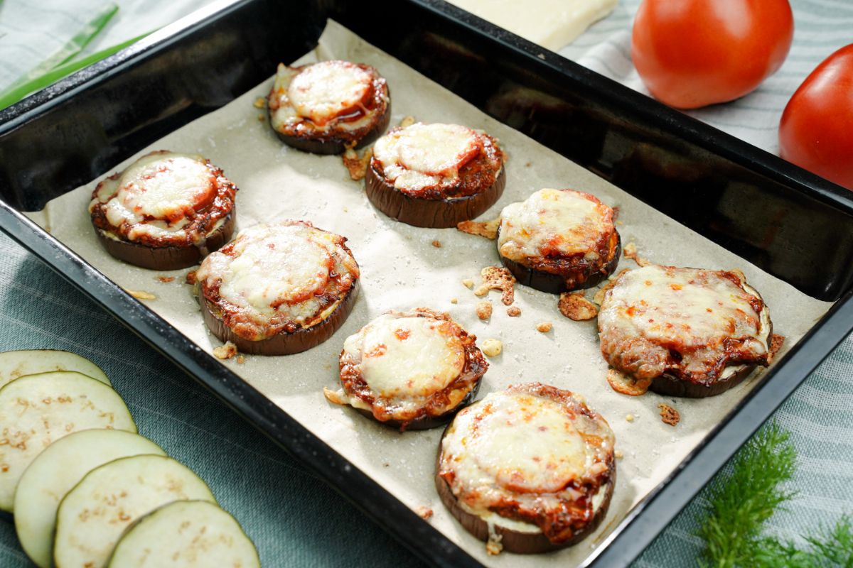 black baking sheet with eggplant pizza rounds on top of parchment paper
