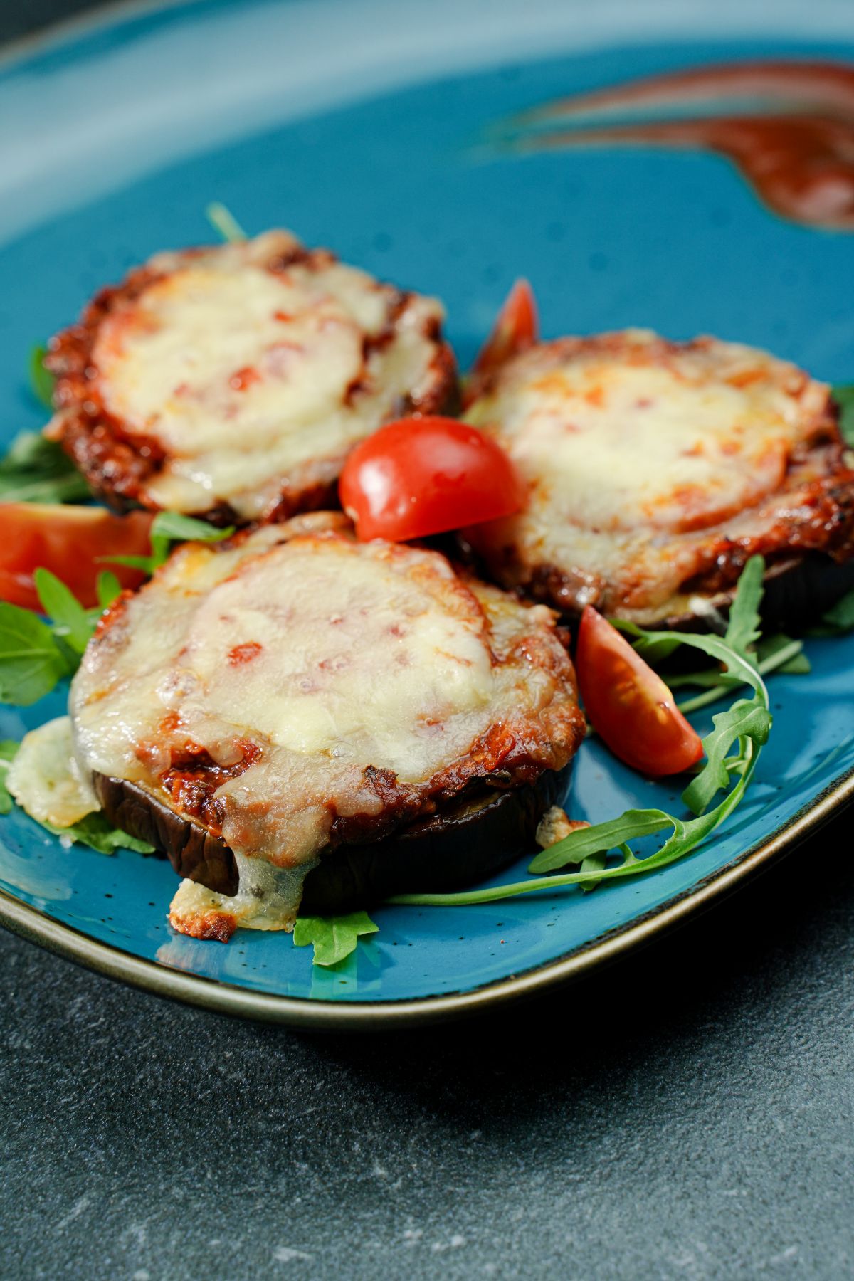 eggplant pizza bites with cheese on top sitting on teal plate