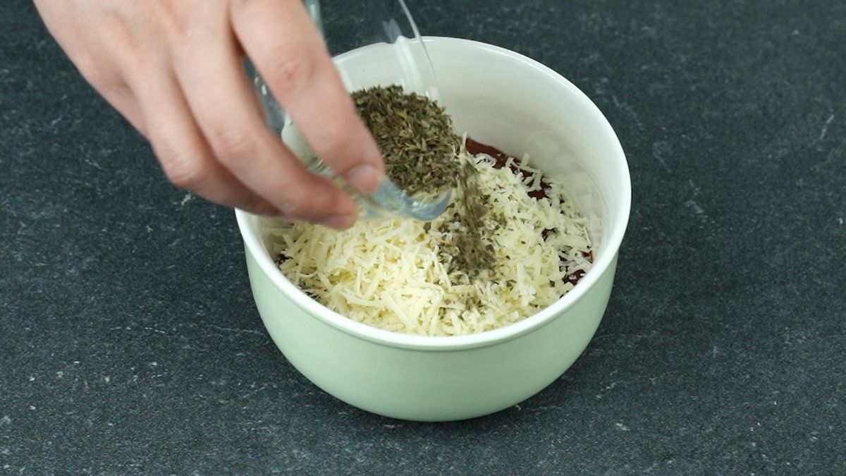 hand adding basil to bowl of cheese and sauce