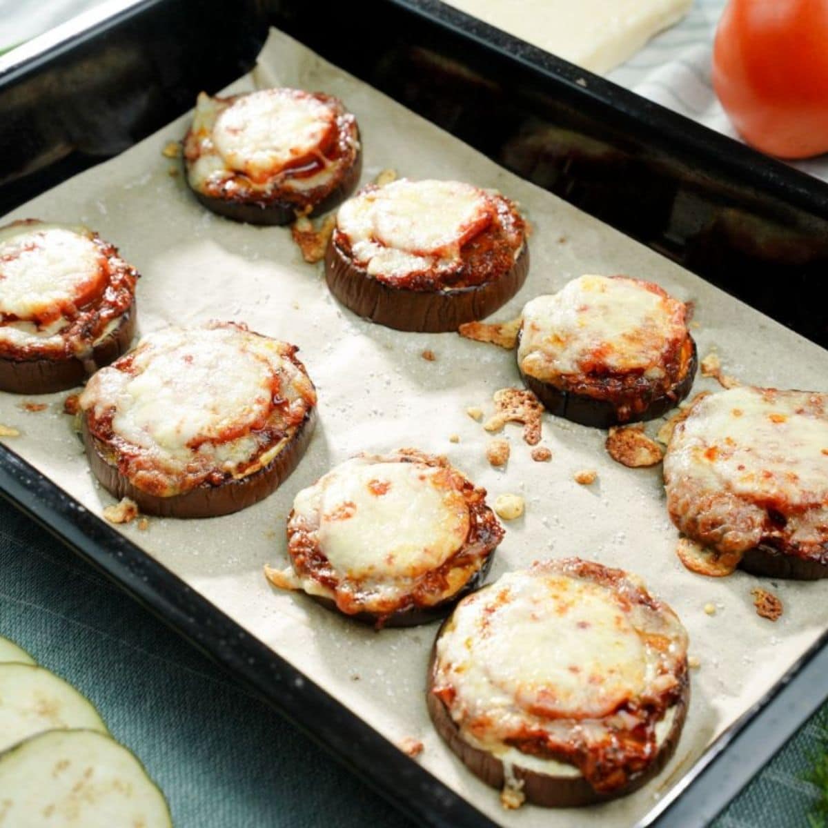 black baking sheet with eggplant pizza rounds on top of parchment paper