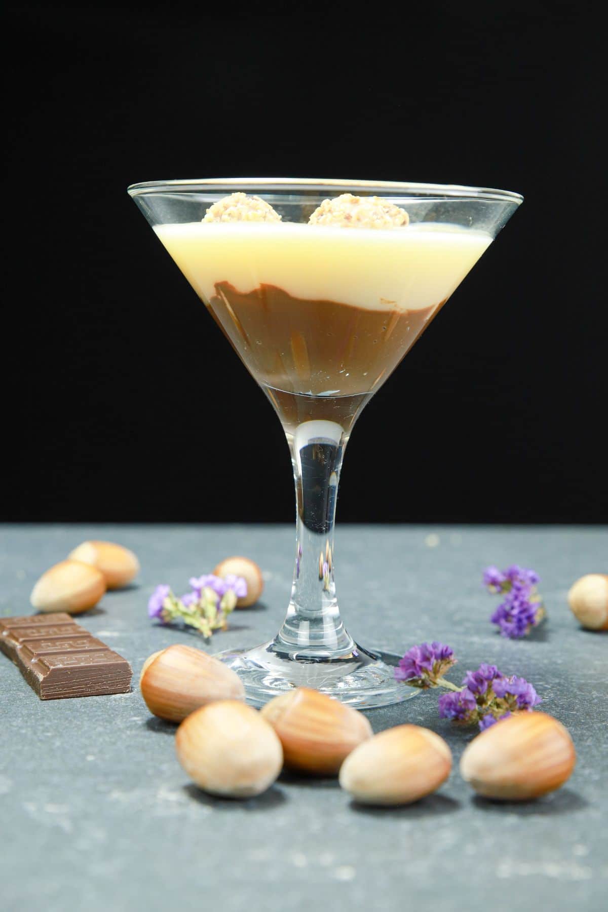 martini glass of layered chocolate and vanilla pudding on table with whole hazelnnuts