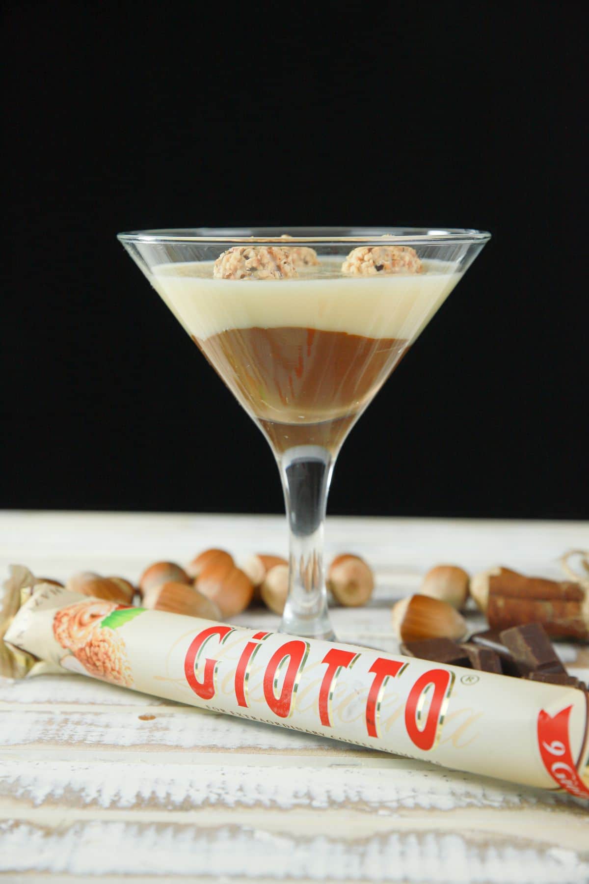 layered kinder joy pudding in martini glass with giotto bar and hazelnuts on white table