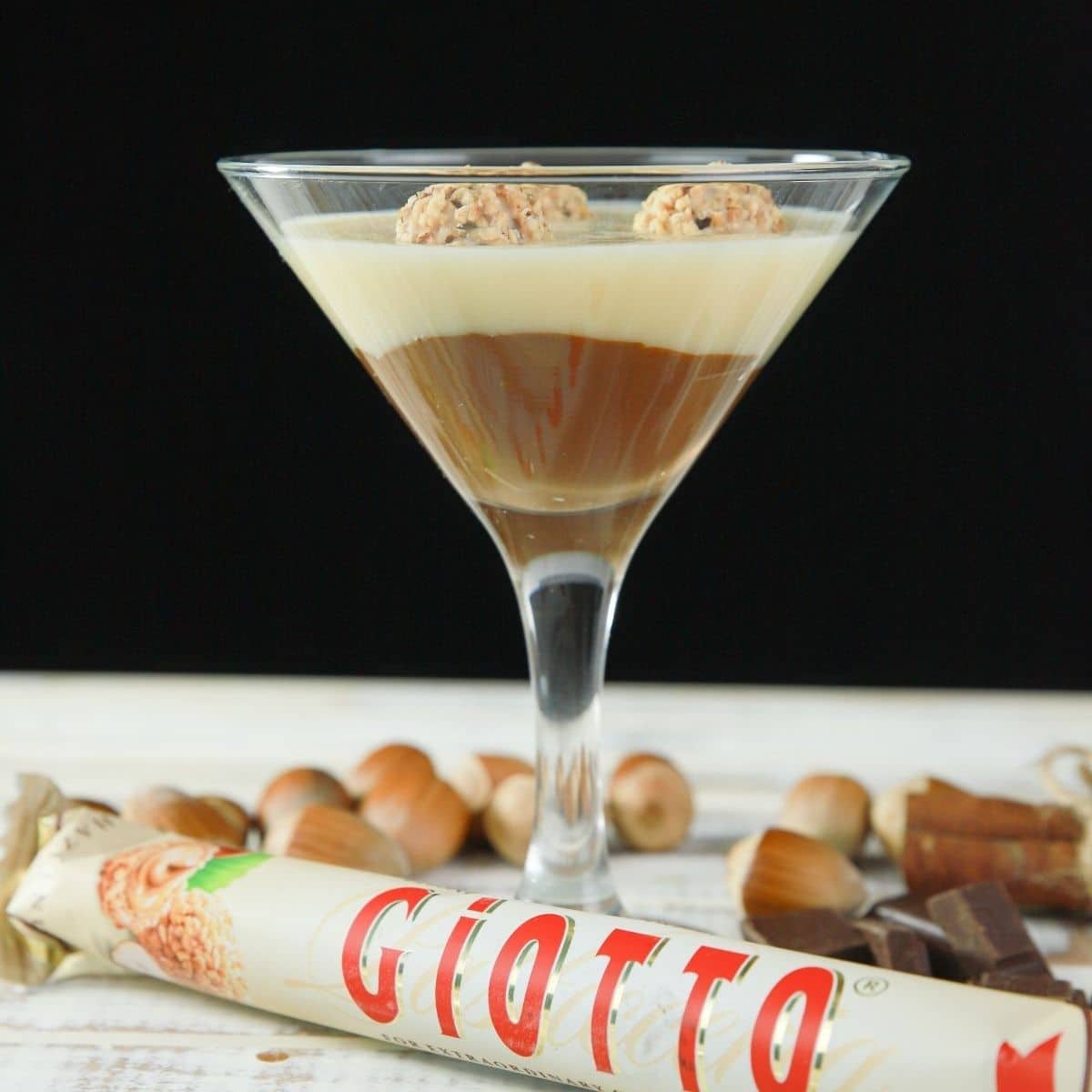 layered kinder joy pudding in martini glass with giotto bar and hazelnuts on white table