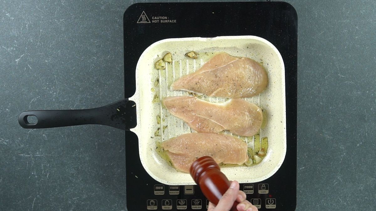 pepper mill hovering over raw chicken in grill pan on hot plate