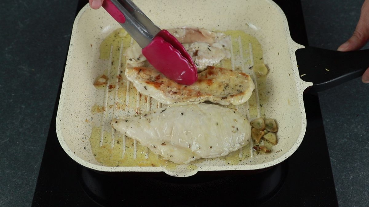 pink tongs turning chicken in grill pan