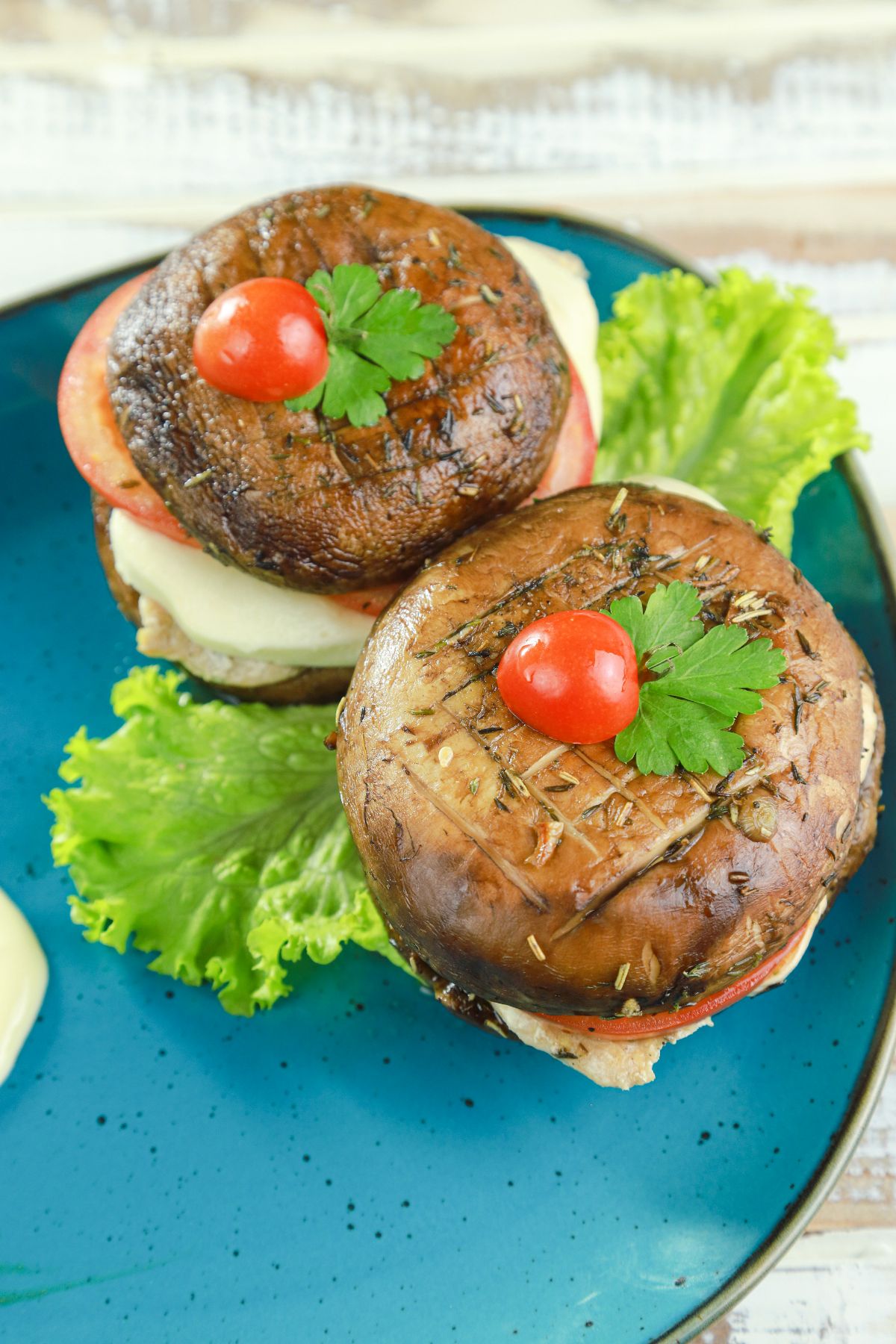 tops of mushroom buns on burgers sitting on lettuce on blue plate