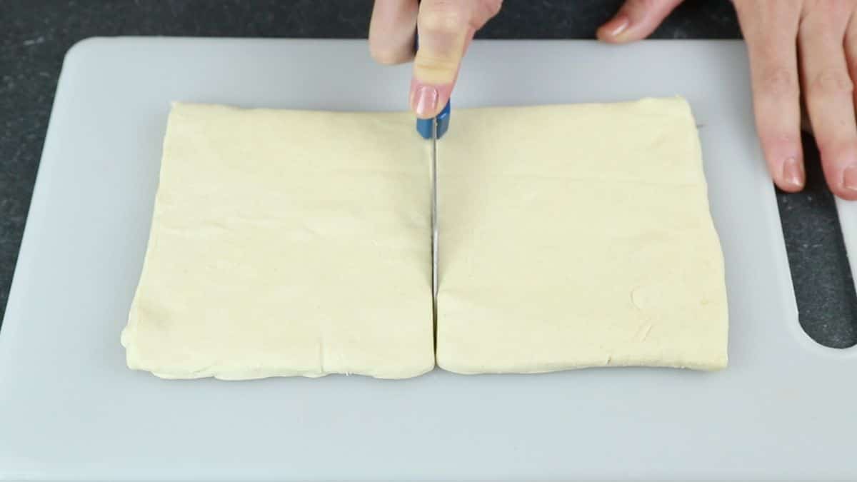 knife cutting puff pastry on white cutting board