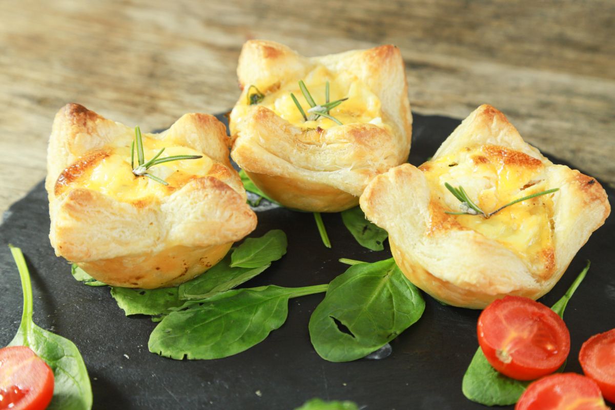 three individual quiche on black plate with spinach and tomato