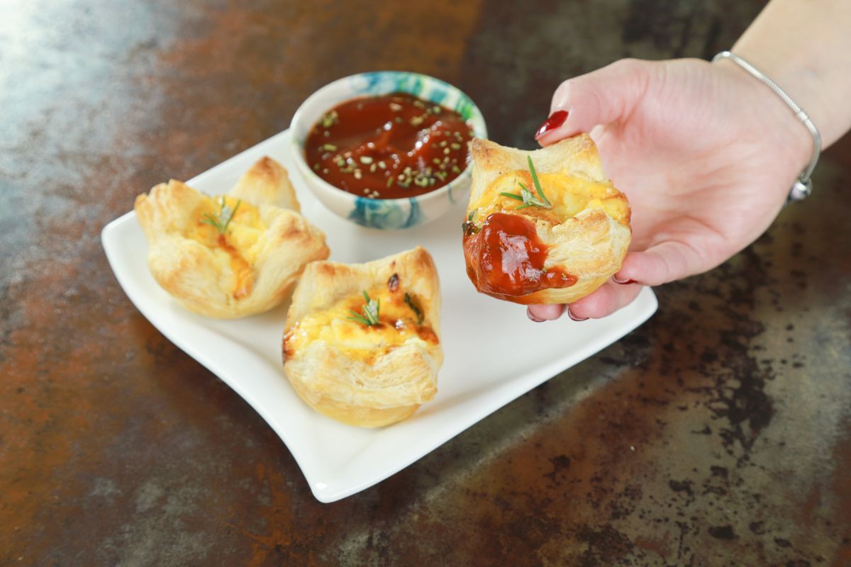hand holding quiche dipped in ketchup above square plate