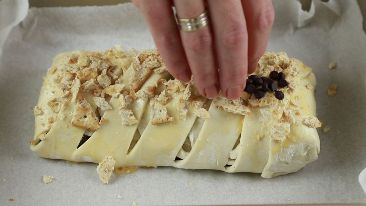 hand putting chocolate chips on top of braided bread