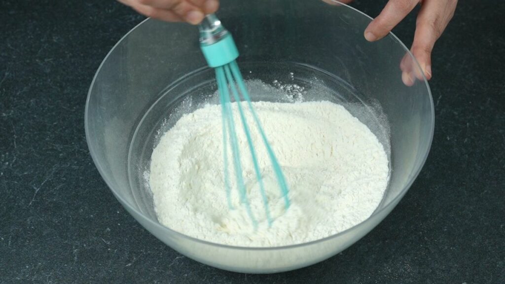 flour and salt whisked in glass bowl with teal whisk