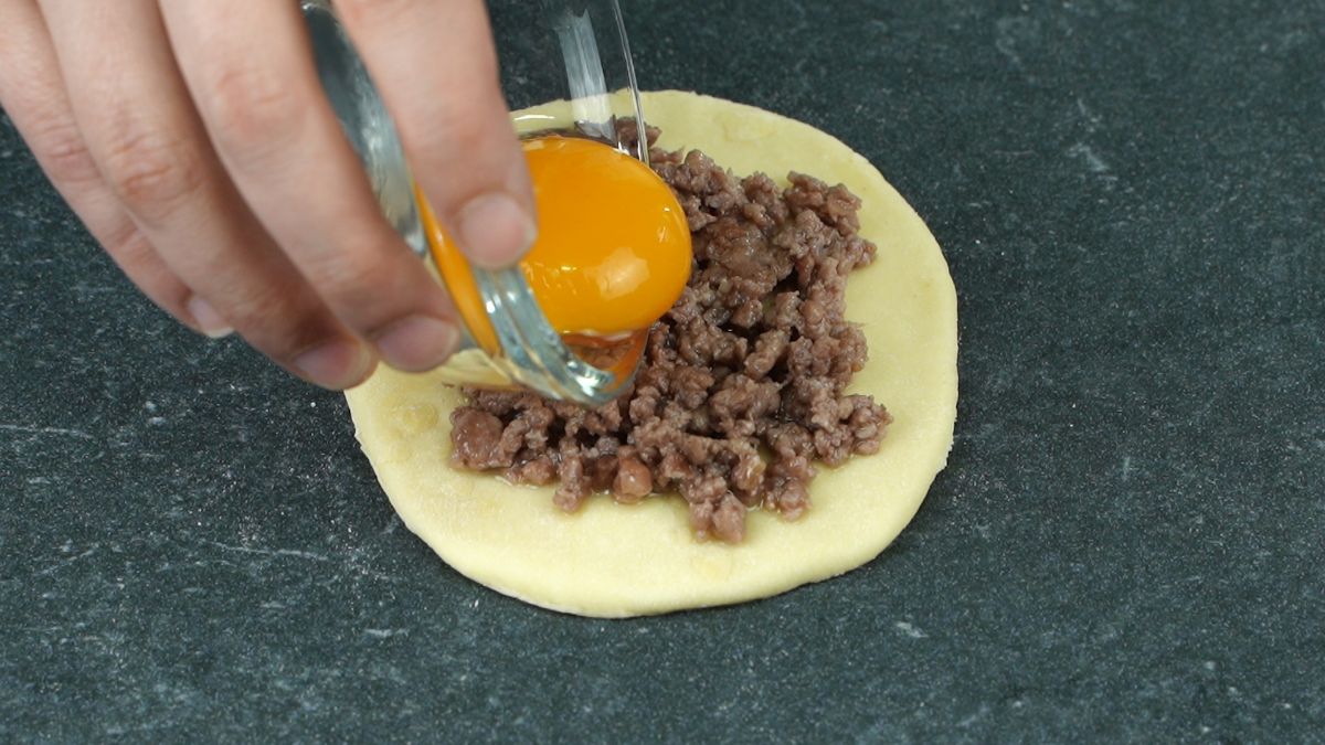 hand putting egg on top of ground beef on dough round