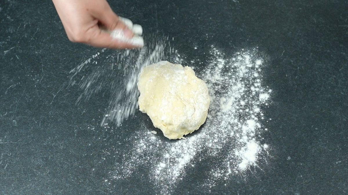 hand sprinkling flour on top of dough ball on black table