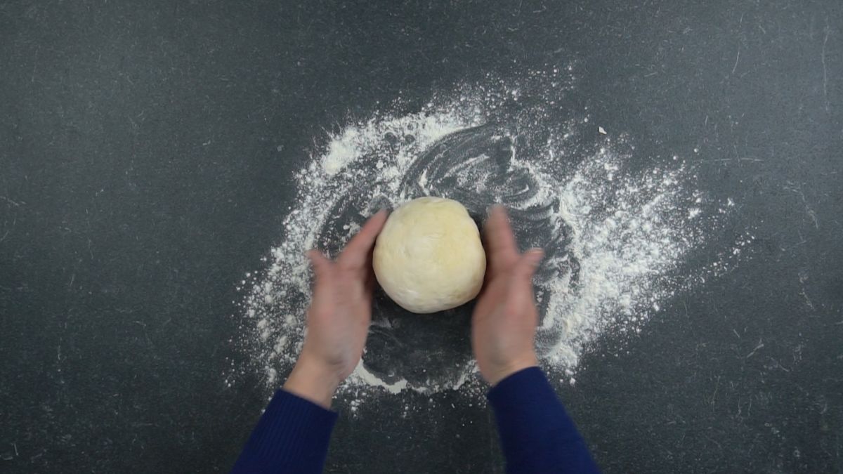 hands holding dough ball above black table