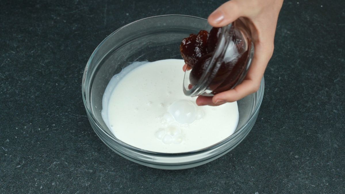 strawberry jam being added to bowl of cream