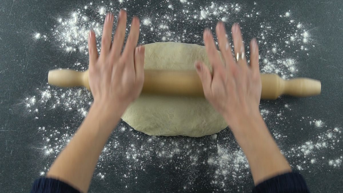 rolling pin being used to roll dough for stromboli