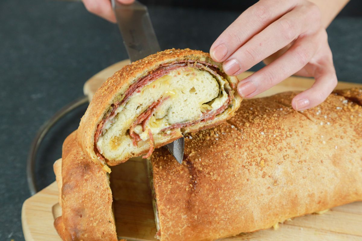 hand holding slice of three meat and cheese stromboli above black table