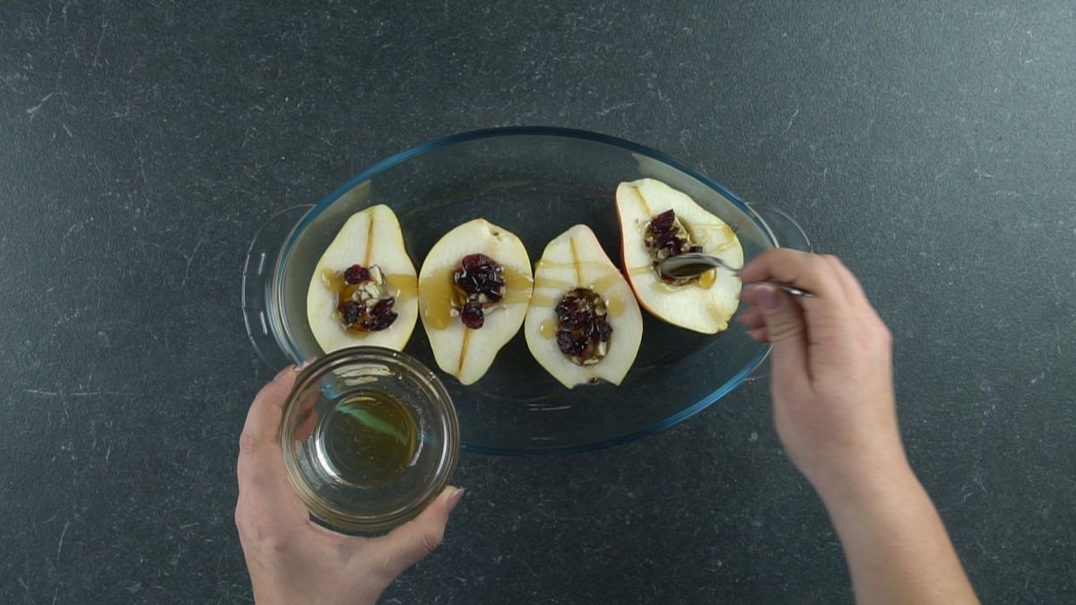 hand pouring honey over top of stuffed pears