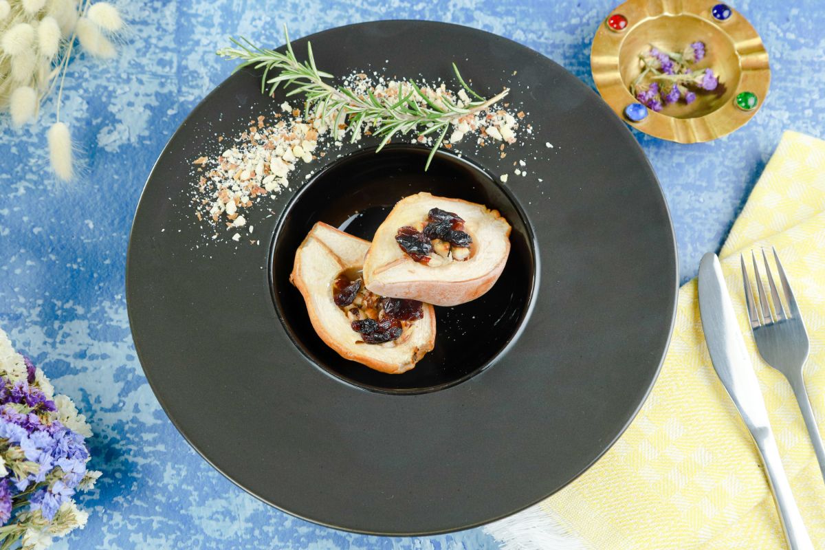 stuffed pears on round black plate on blue table with yellow napkin on right topped with utensils
