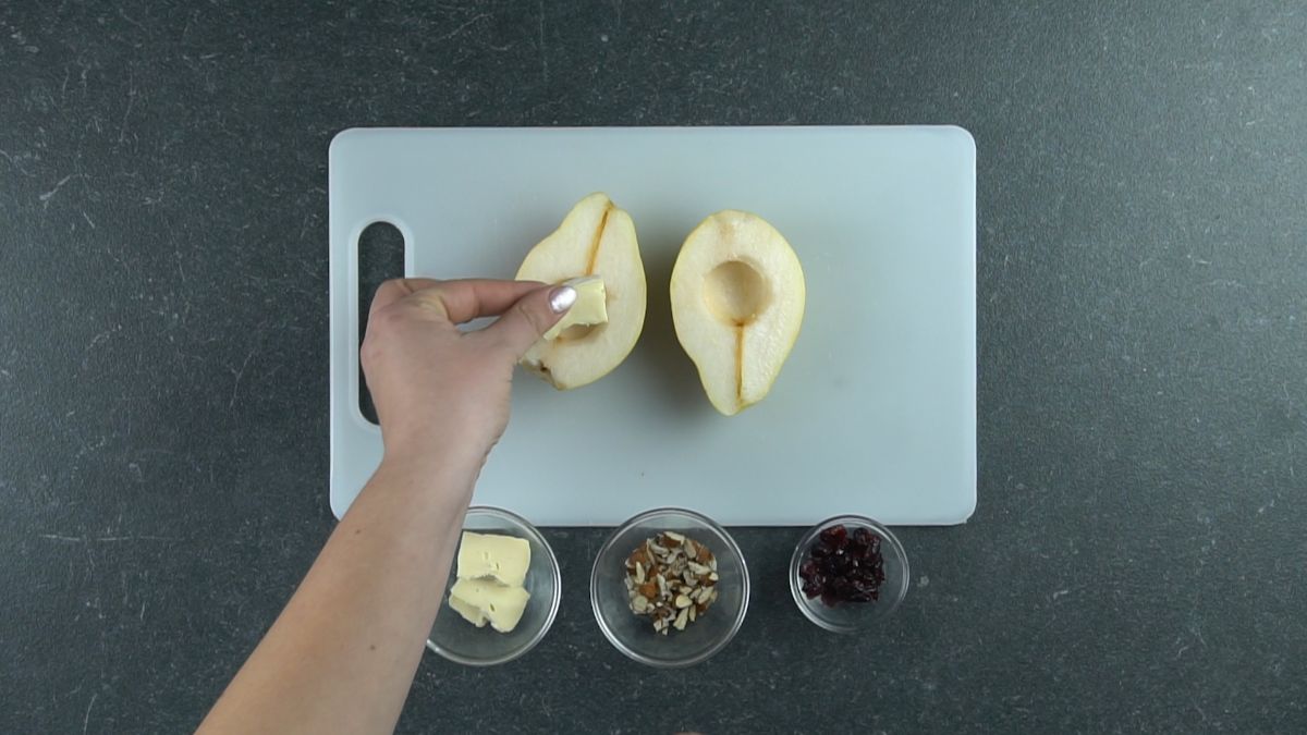 hand putting brie into pear halves on white cutting board
