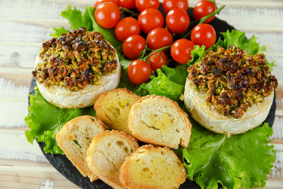 two baked brie rounds topped with nuts on black plate with lettuce tomato and bread slices