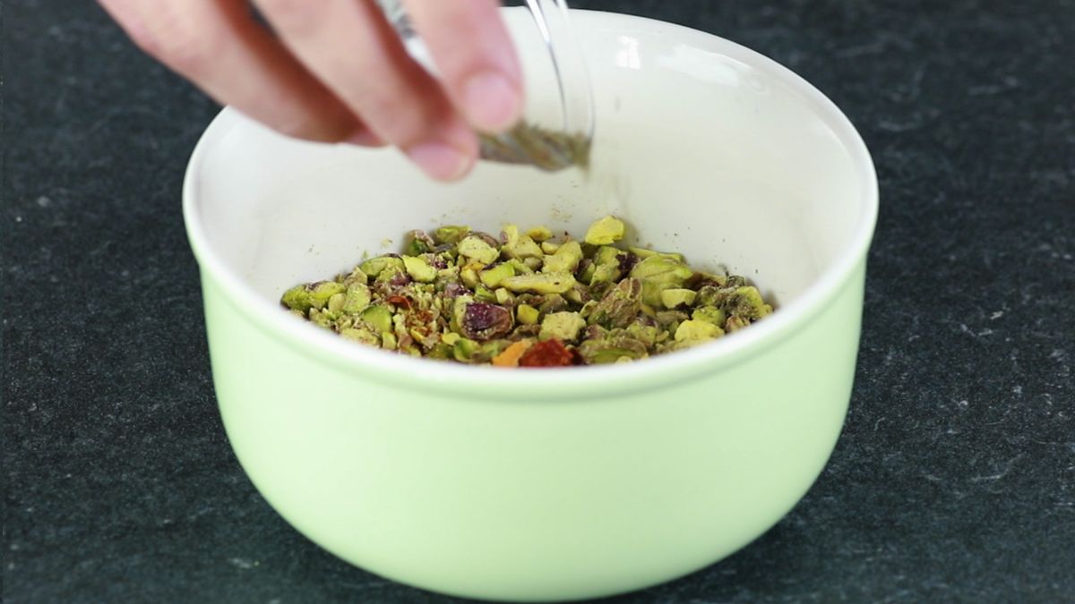 white bowl of pistachios with herbs being added