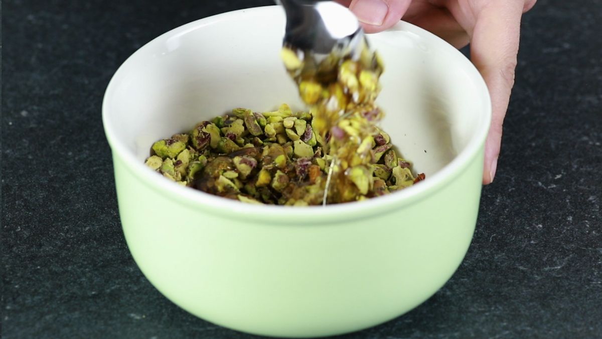 spoon stirring pistachios and honey in white bowl
