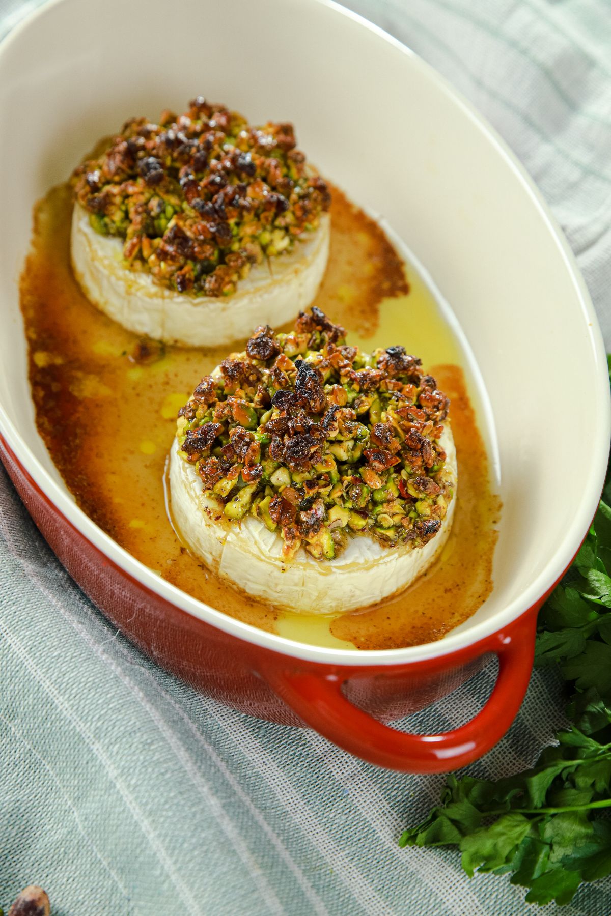 brie topped with pistachios in white and red oval baking dish on striped tablecloth