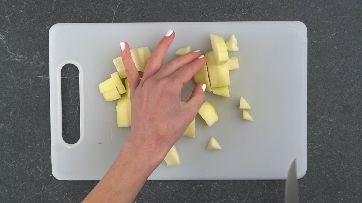 hand cutting apple pieces on white cutting board