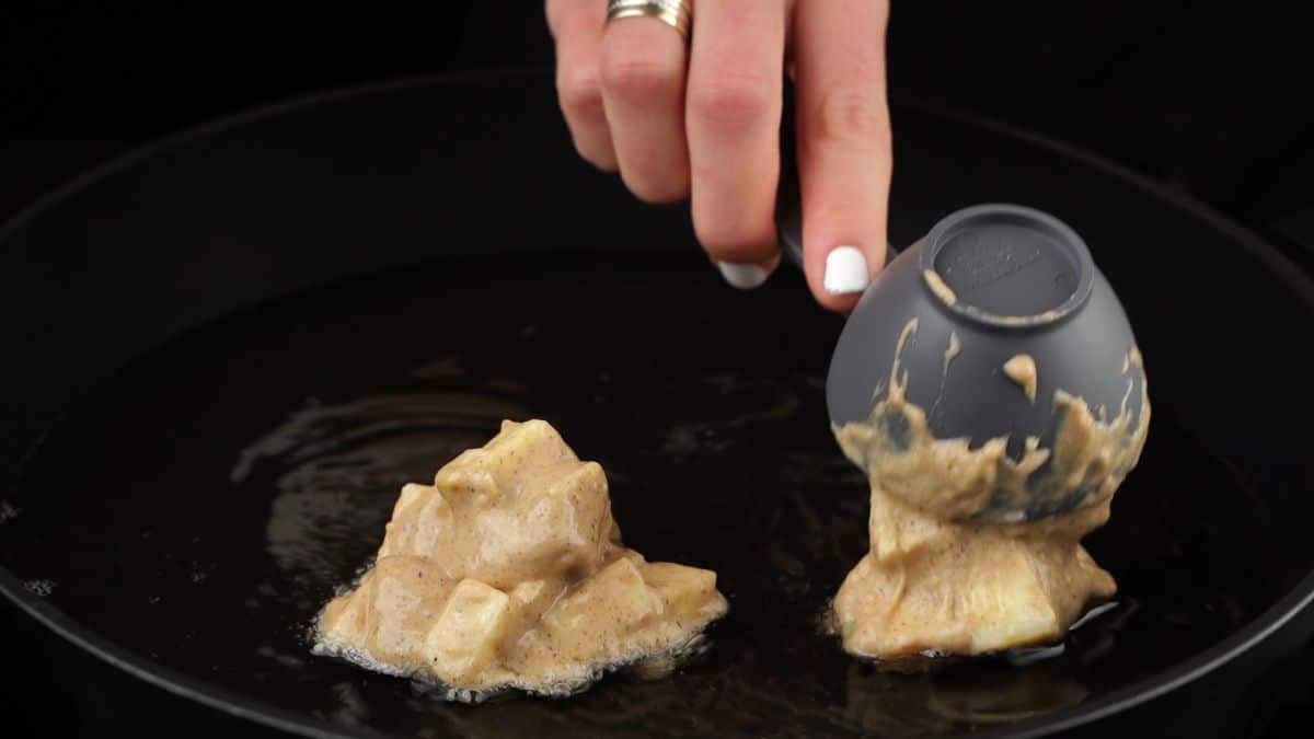 hand scooping apple fritter batter into hot oil