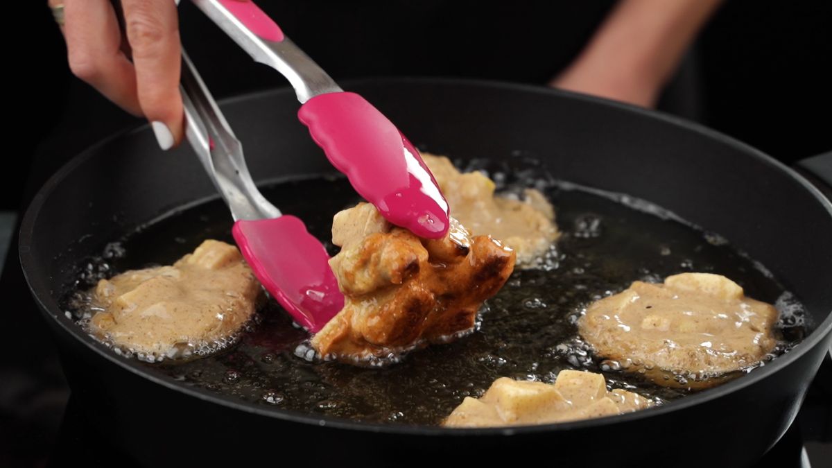 pink tongs turning fritter over in hot oil