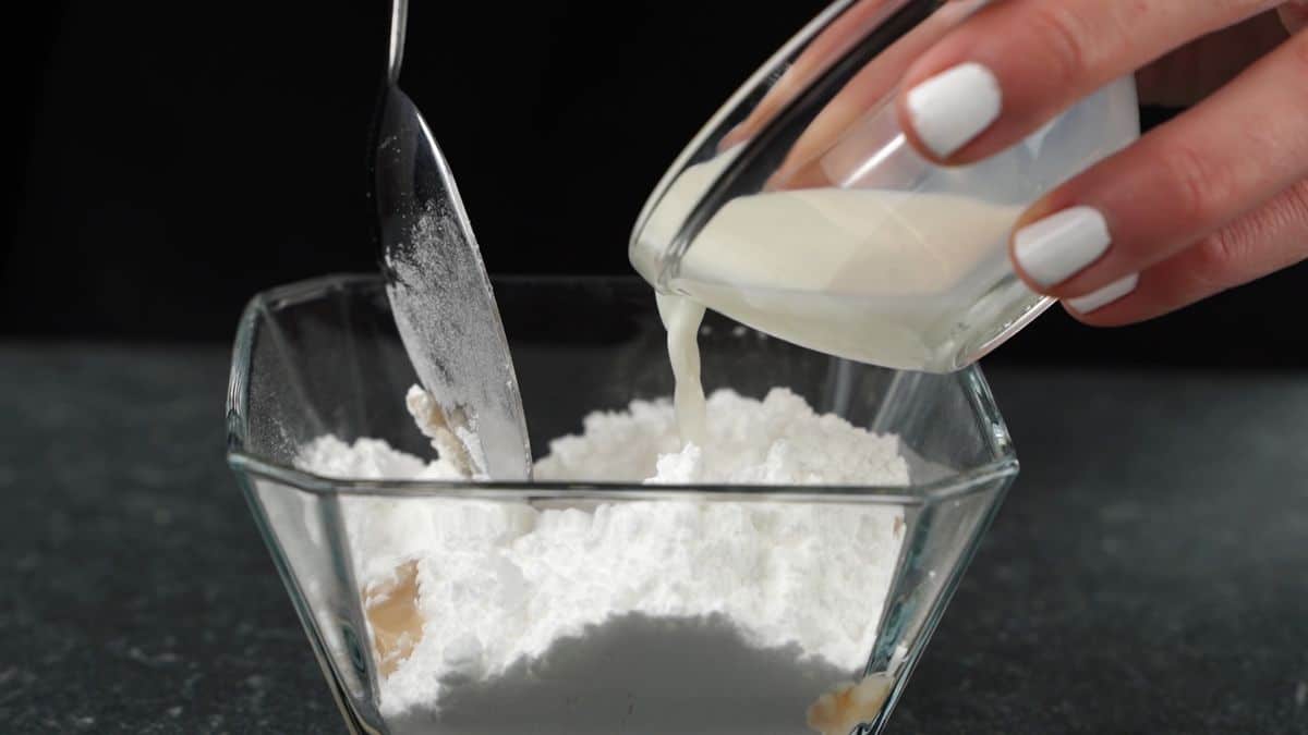 adding milk into glass bowl of powdered sugar