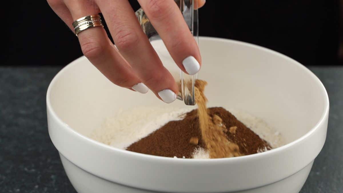 hand adding spices into white bowl