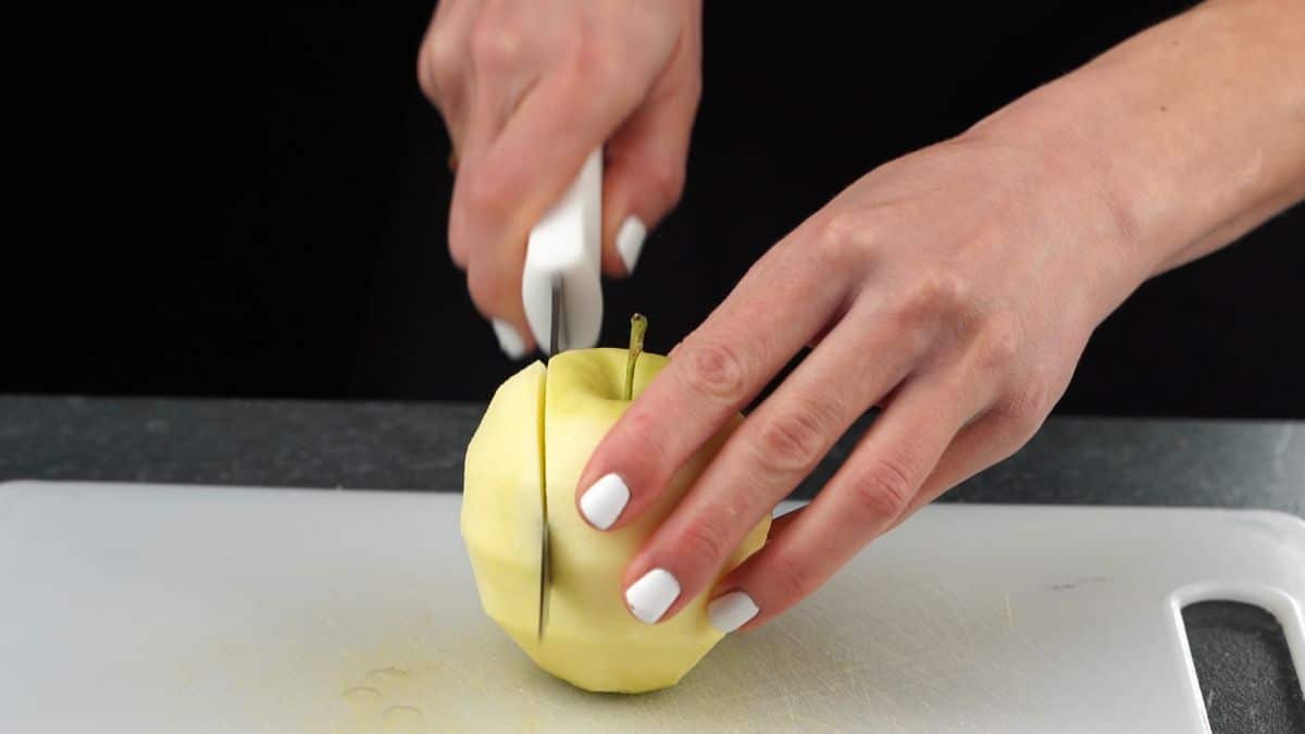 hand cutting a peeled apple on white cutting board