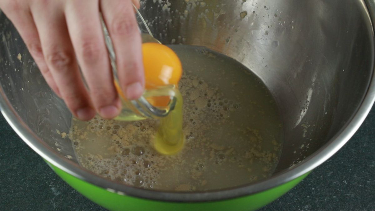 egg in small glass bowl being held above bowl with yeast mixture