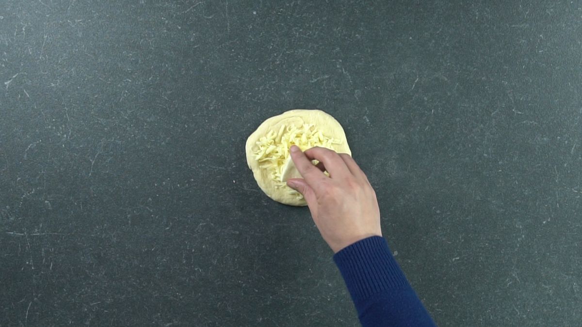 hand in blue shirt adding cheese to dough round