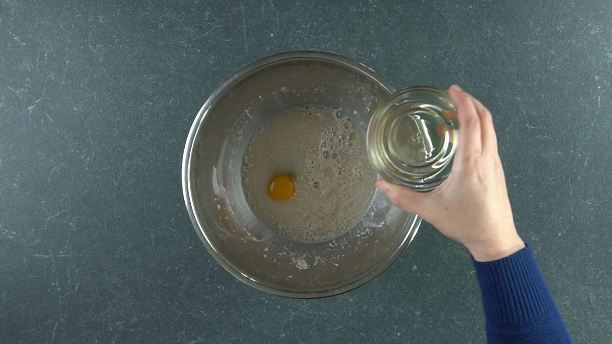 glass bowl in hand held above silver bowl with yeast water and egg