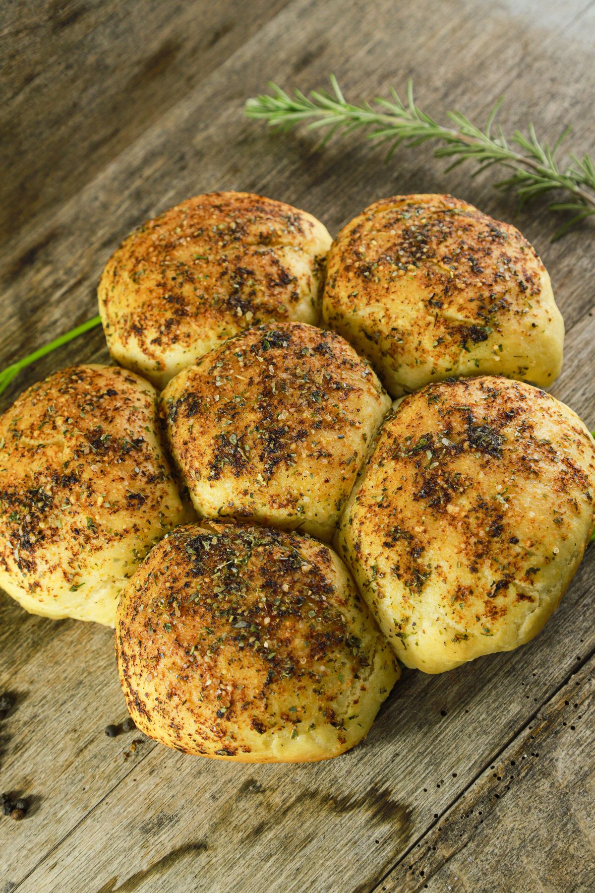 herb topped golden bread rolls on wood table