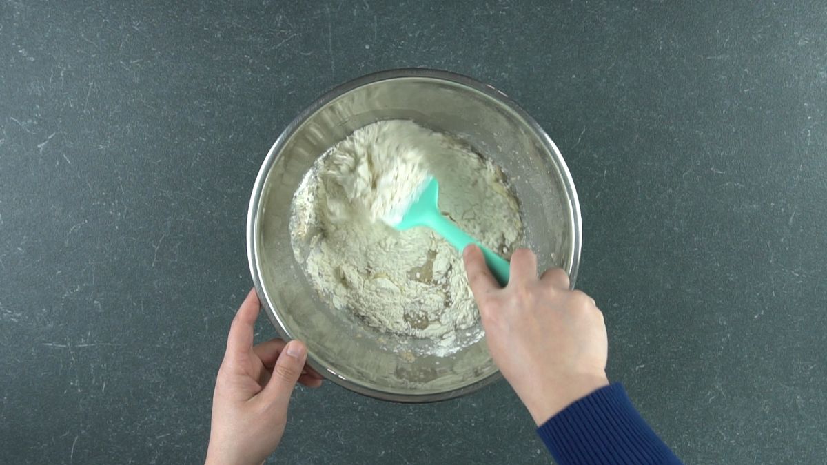 blue spatula stirring dough in silver bowl
