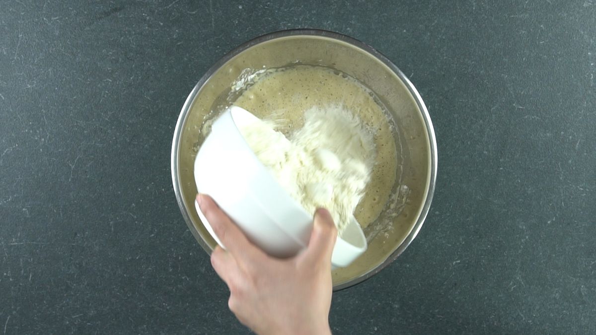 white bowl of flour being poured into silver bowl with dough
