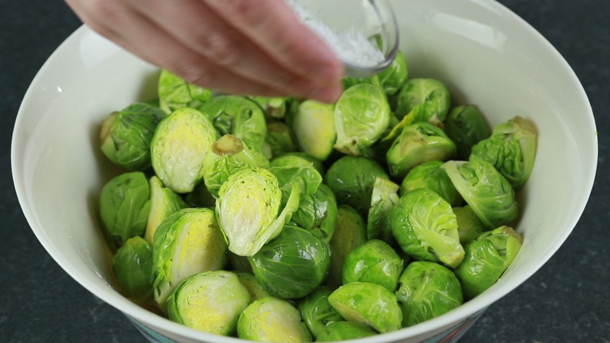 hand adding oil onto brussels sprouts