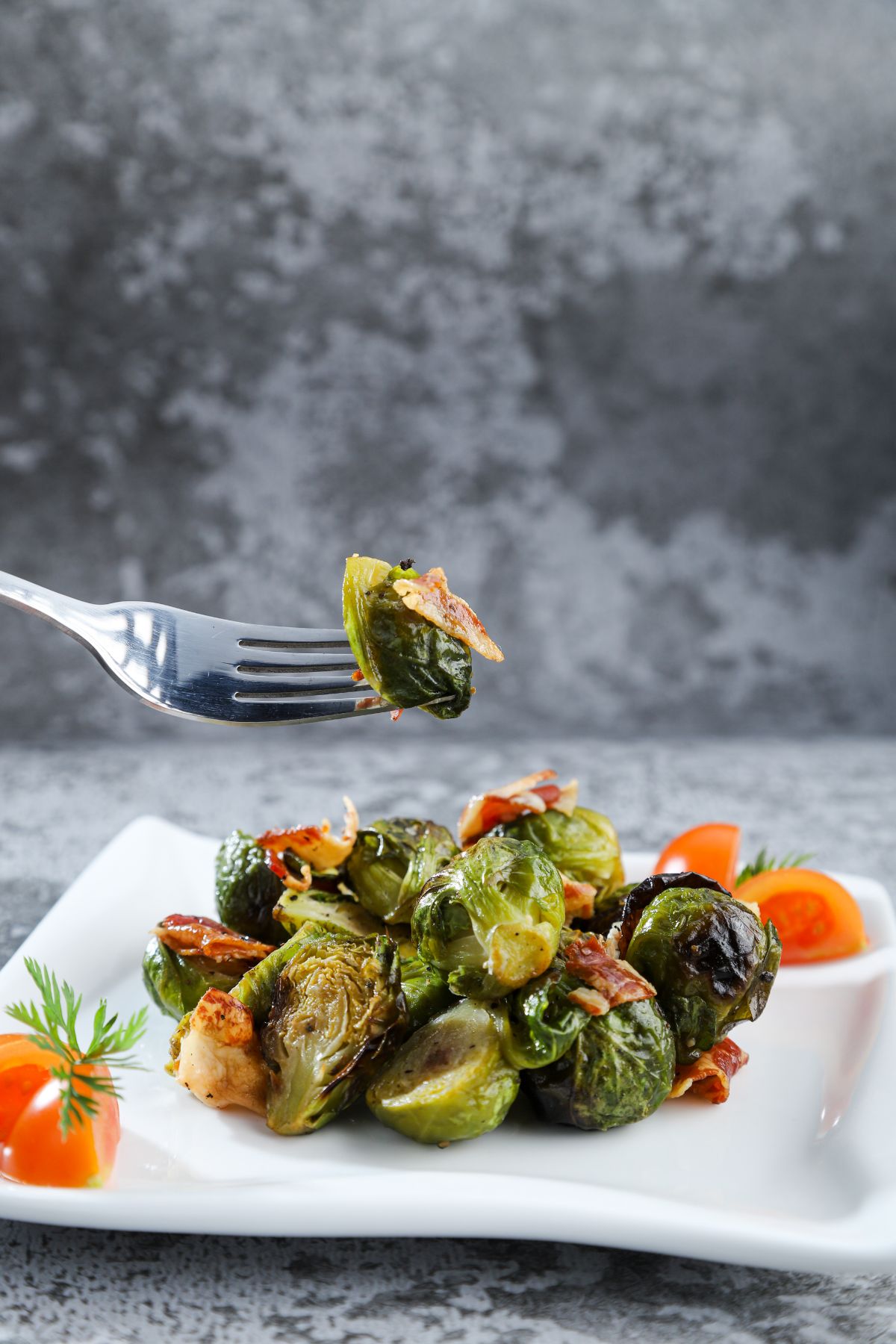 Brussel sprout on fork hovering above white plate with grey background