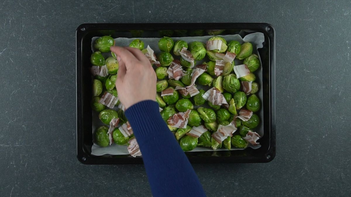 hand putting bacon on top of Brussels sprouts