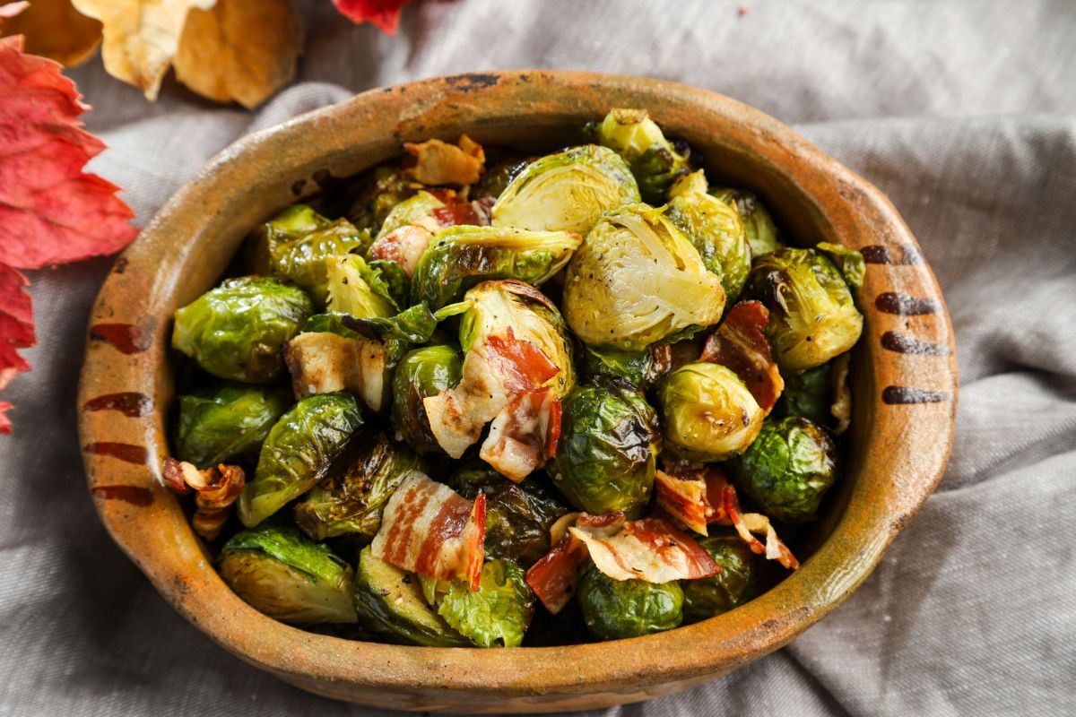 brown bowl of roasted Brussels sprouts with bacon on grey tablecloth