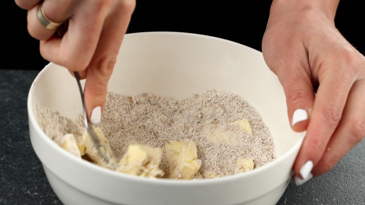white bowl of crumble with butter being mixed in using a fork