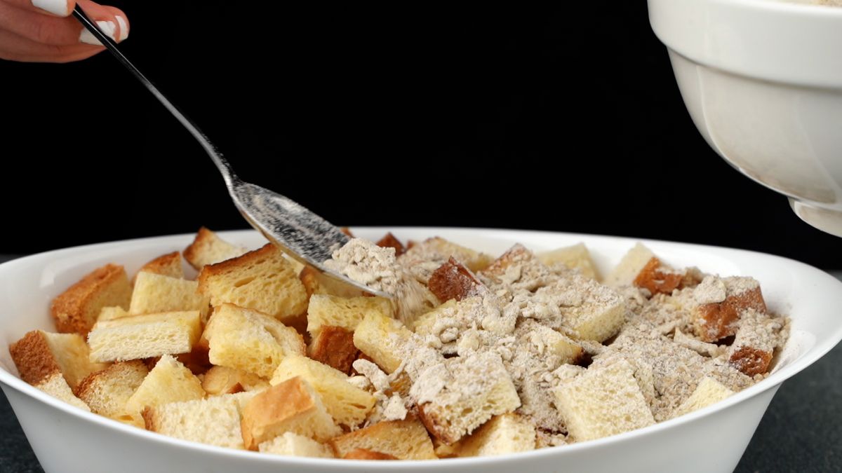 spoon adding crumble on top of white oval bowl of french toast bake